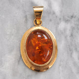 Yellow gold pendant with an oval amber in a rub over setting. 