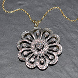 Silver floral pendant with diamonds on a gold chain against a gray background