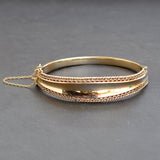 Yellow gold concave graduated bangle with a fancy edge and safety chain.