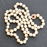 A vintage pearl necklace with a yellow gold clasp and a central garnet piece, displayed against a dark background.