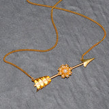 Gold necklace with arrow and floral design on a gray surface