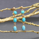 Gold earrings with turquoise stones on a gold branch against a gray background