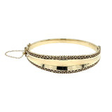 Yellow gold concave graduated bangle with a fancy edge and safety chain.