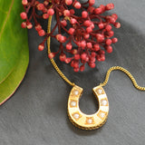 Gold horse shoe necklace set with seven cultured pearls on a chain. Circa 1900.