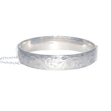 A vintage silver bangle with intricate pattern engraving, attached with a safety chain.